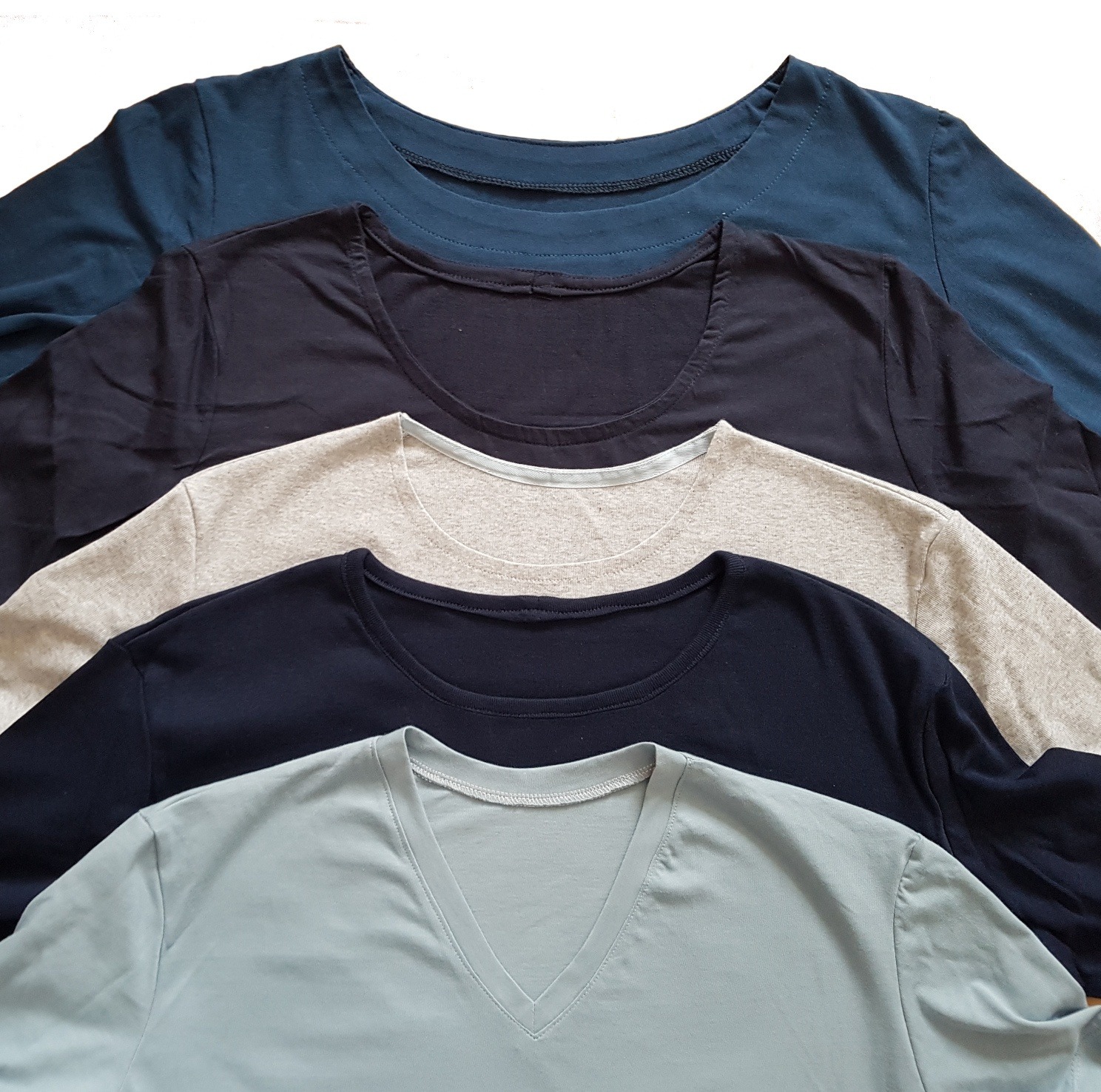5 T-Shirts, alle in Blau- und Grautönen. Die Halsausschnitte sind versetzt übereinandergelegt. Alle Ausschnitte sind anders verarbeitet.