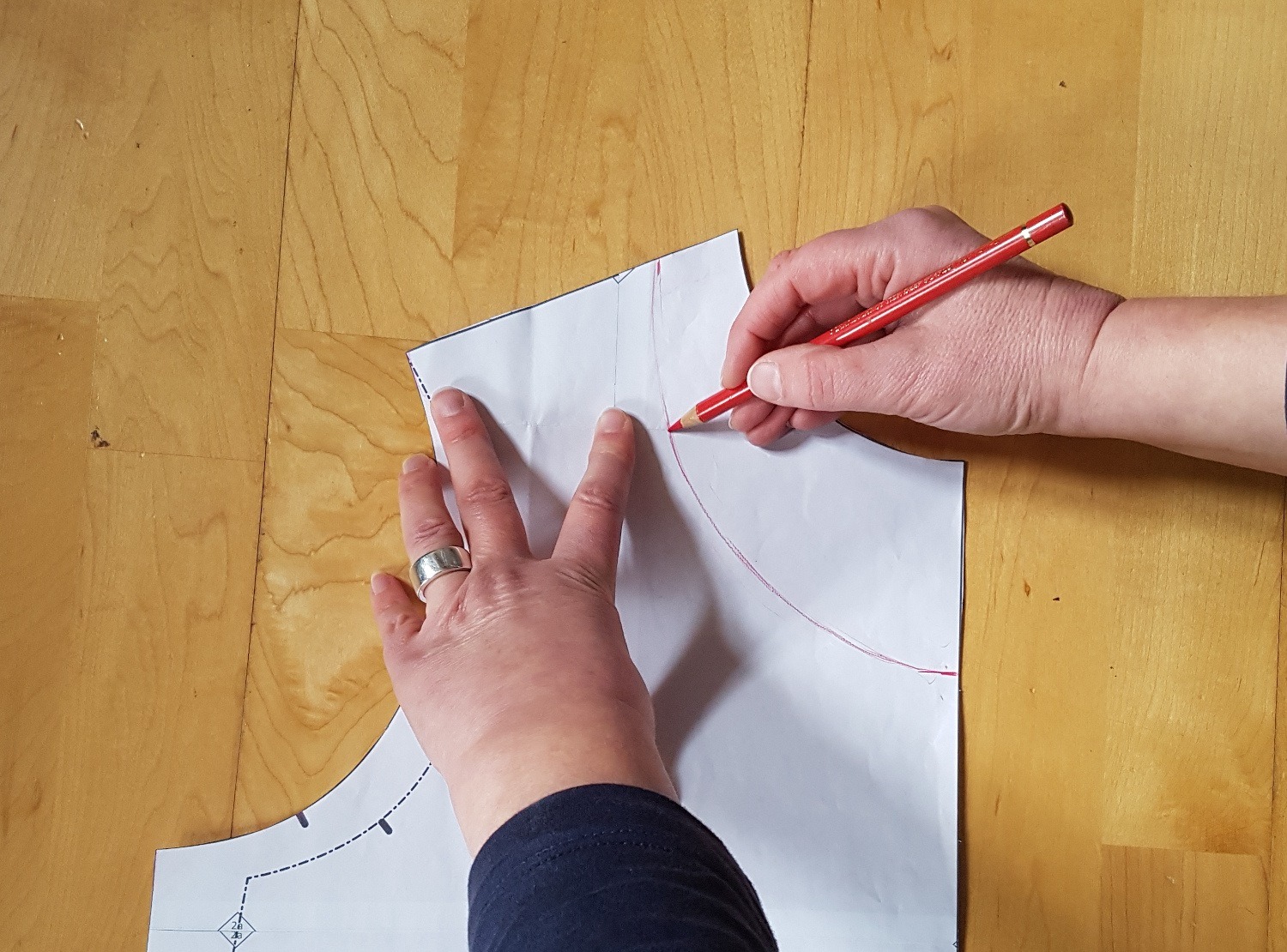 Mit einem roten Stift zeichnet Sabine die neue Ausschnittform auf das Vorderteil-Schnittteil. Sie verbindet die Punkte in der vorderen Mitte und am Schulterpunkt mit einer schönen Kurve.