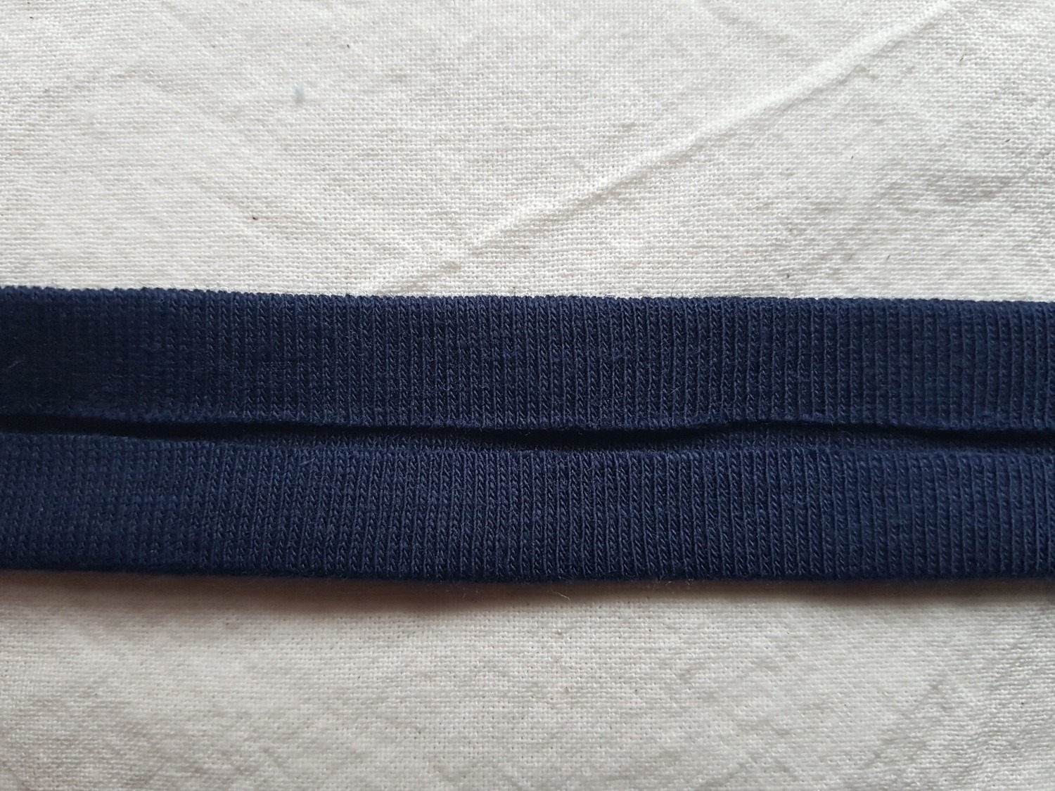 Ein dunkelblauer Stoffstreifen vor weißem Hintergrund. Die Längsseiten des Streifens sind jeweils 1 cm nach innen gebügelt.
