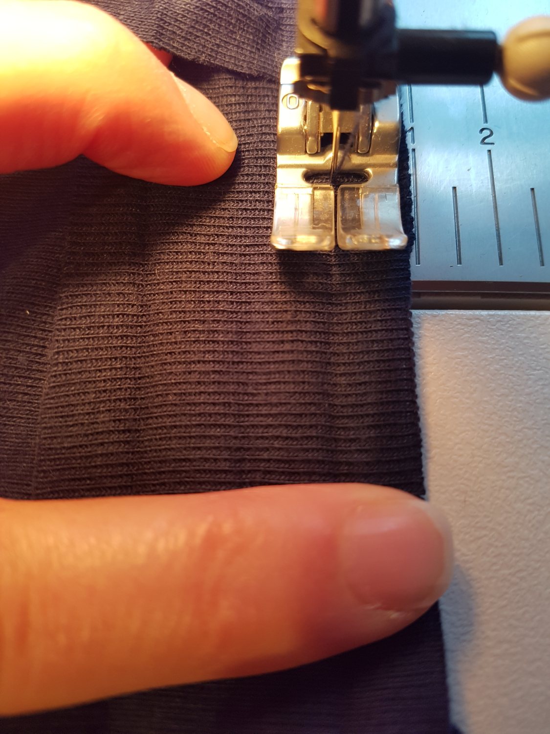 Der Streifen liegt auf dem Halsausschnitt unter der Nähmaschine. Die Nadel sticht im gebügelten Falz ein.
