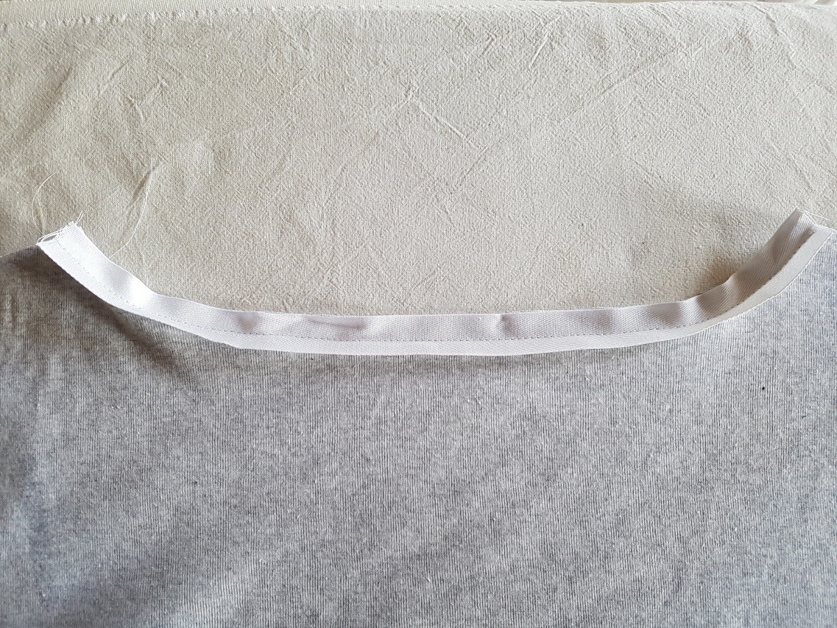 Grau-meliertes Rückenteil auf Nessel-Hintergrund. Ein weißes Band ist an der Halsausschnittkante angenäht.