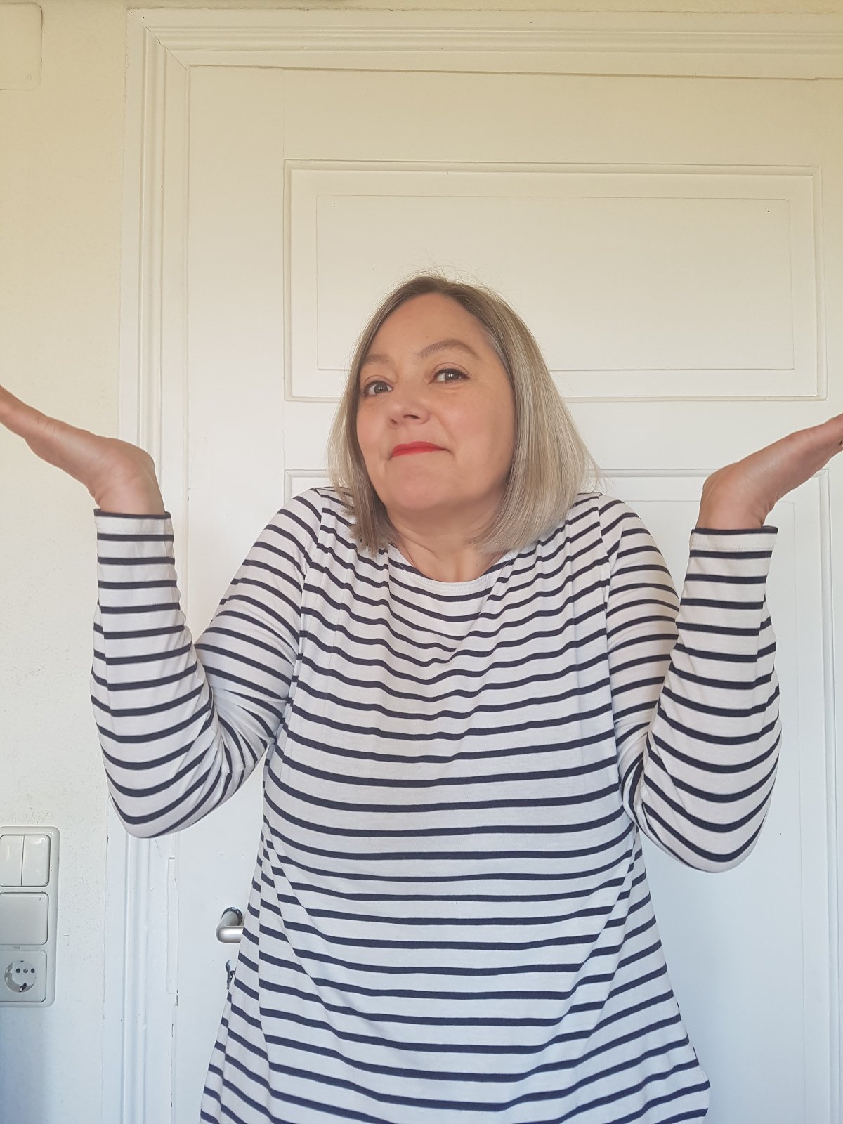 Sabine_nachdenklich3 Sabine im Ringelshirt, vor einer weißen Tür, ratlos mit hochgezogenen Schultern.