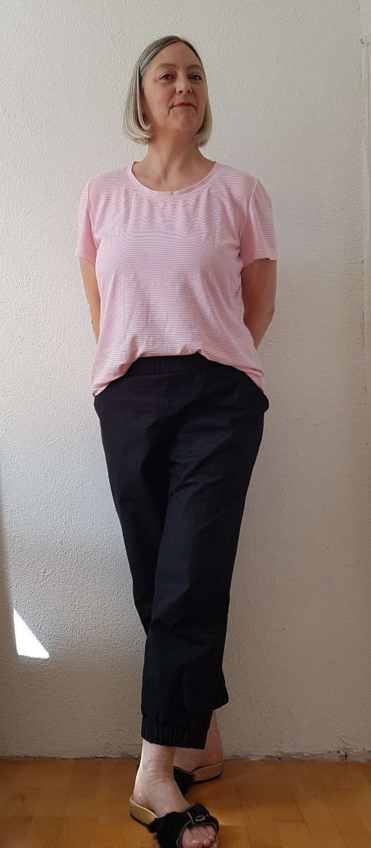 Sabine in rosa T-Shirt und der neuen schwarzen Hose vor weißer wand