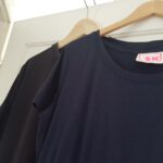 beide Kleider hängen jeweils auf einem Bügel übereinander an einer Tür. Das neue Kleid überdeckt das alte. Man sieht nur ein Teil des Halsausschnitts und einen Ärmel.