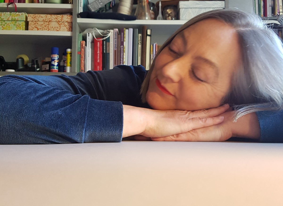 Sabine mit geschlossen augen und Kopf auf den Händen auf dem Tisch. Sie sieht aus, als würde sie am liebsten auf dem Tisch übernachten.