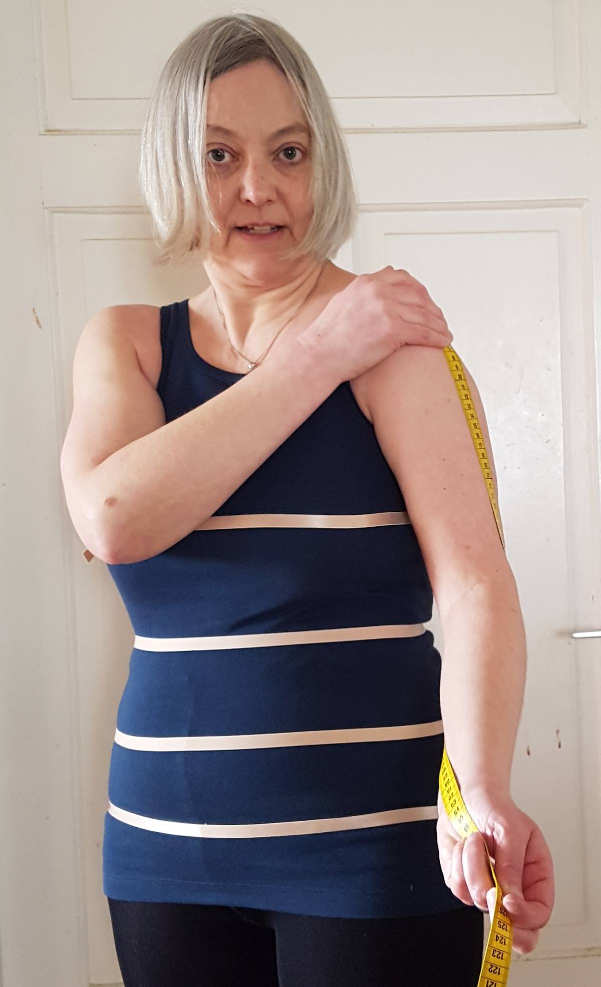 Ärmellänge messen Sabine hält den Anfang des Maßbandes auf Schulterhöhe. Das Maßband verläuft am leicht gebeugten Arm bis zum Handgelenk.