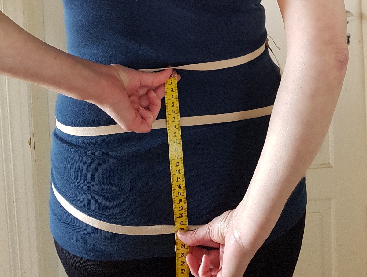 Hüfttiefe messen Sabine von hinten. Mit der linken halt hält sie den Anfang des Maßbandes auf Taillenhöhe, mit der rechten Hand markiert sie auf dem Maßband, wo die Hüftlinie sitzt.