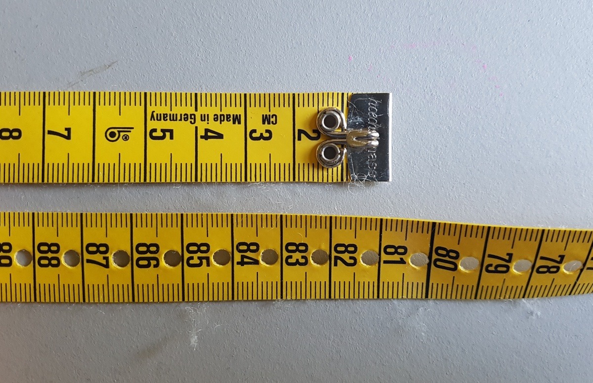 Man sieht den Anfang des Maßbands mit einem kleinen Haken, und den Mittelteil, mit kleinen Löchern, wo man den Haken einhängen kann